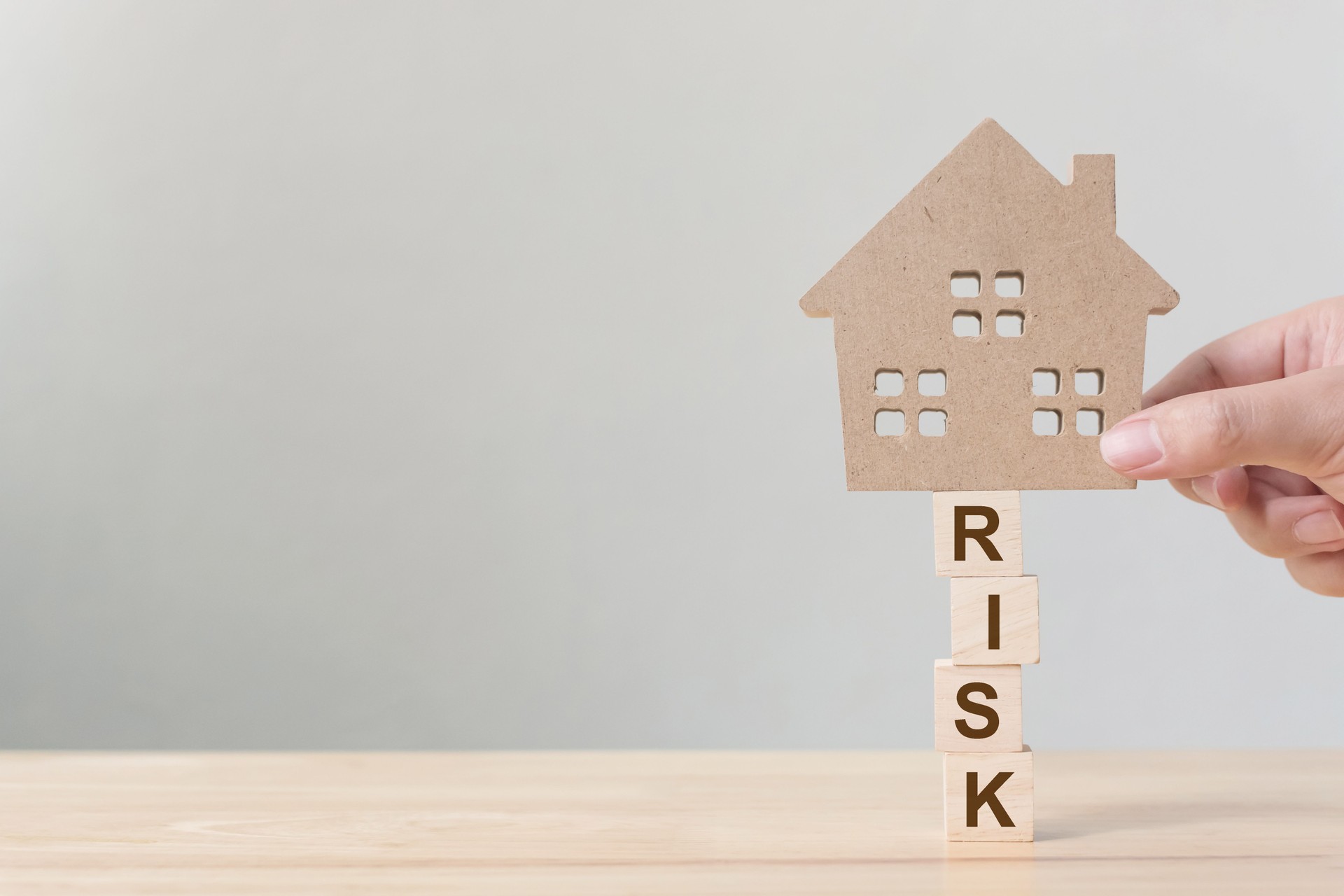 Property investment and house mortgage financial. Risk management concept. Hand putting wooden home on wood block with word "risk"